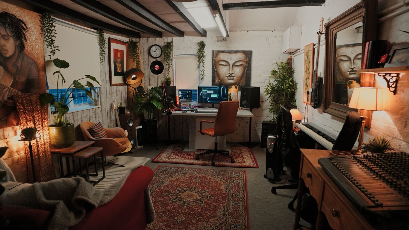 The Studio: a lamp-lit room with exposed brick, plants, rugs, studio monitors and a piano along the far wall.